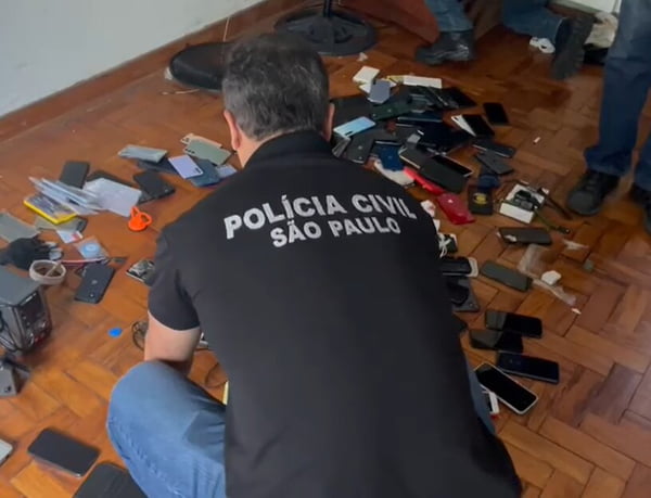 Foto colorida mostra policial se debruçando sobre celulares roubados espalhados pelo chão; número de furtos sobe em São Paulo - Metrópoles