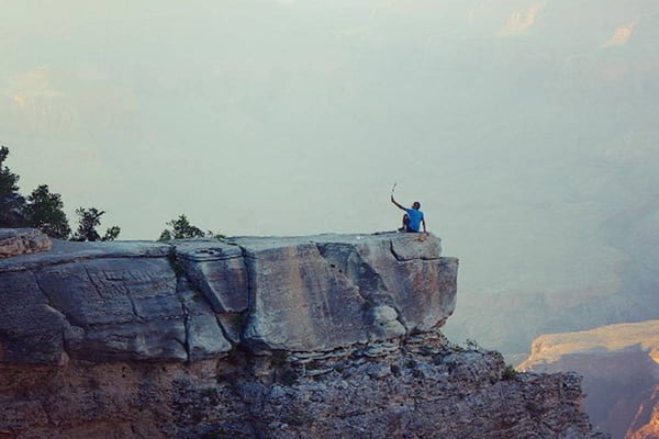 Imagem colorida de pessoa na beira de montanha para tirar selfie - Metrópoles