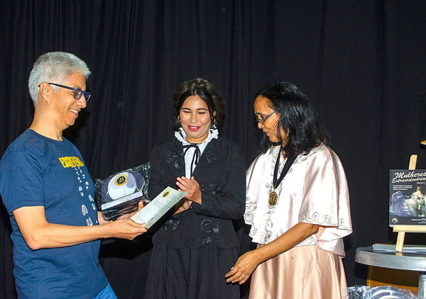 Fotografia colorida mostrando homem recebendo prêmio de duas mulheres-Metrópoles