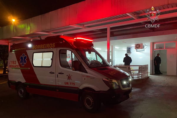 Imagem colorida de ambulância dos bombeiros, em frente a entrada de hospital, à noite, com sirene acesa
