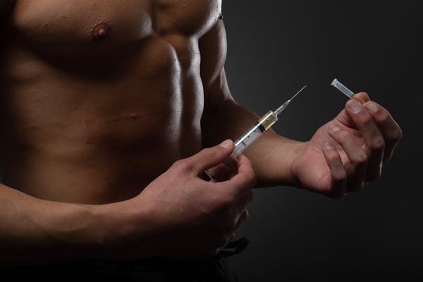 Foto mostra homem musculoso com agulha nas mãos, ilustrando o uso de anabolizantes