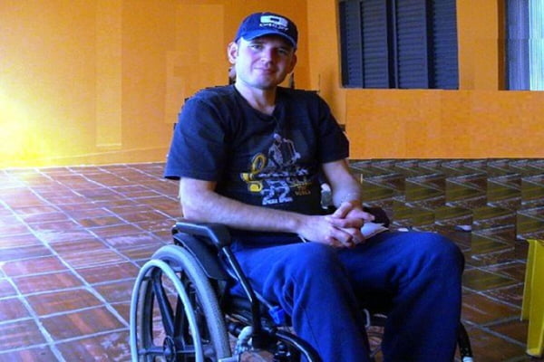 Em foto colorida homem branco com calça e camiseta azuis sobre cadeira de rodas - Metrópoles
