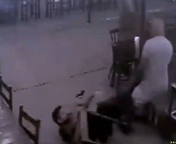 Imagem de um homem caído entre cadeiras apontando arma para outro, de pé - Metrópoles