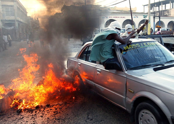 Imagem colorida de rebeldes haitianos em carro em rua pegando fogo - Metrópoles