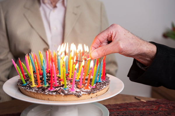 Pessoa segurando bolo de aniversário com várias velas coloridas acesas - Metrópoles