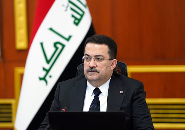 Imagem colorida mostra primeiro-ministro do Iraque sentado em frente da bandeira iraquiana - Metrópoles