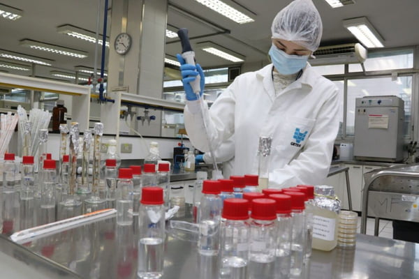 Imagem de mulher com touca, máscara e jaleco branco manuseando pepita em laboratório - Metrópoles