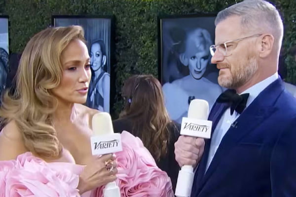 Jennifer Lopez no Globo de Ouro com um vestido rosa e segurando um microfone - Metrópoles