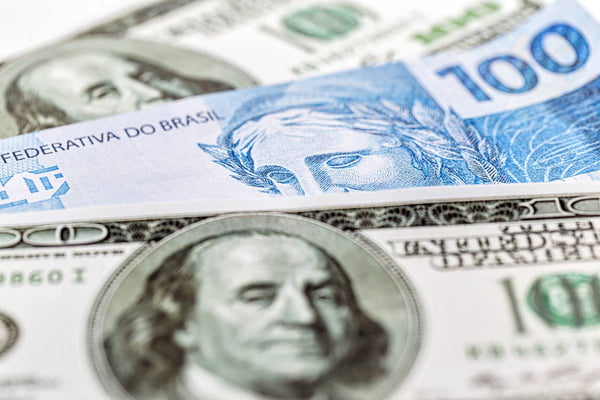Imagem colorida de notas de dólar e de real - Metrópoles