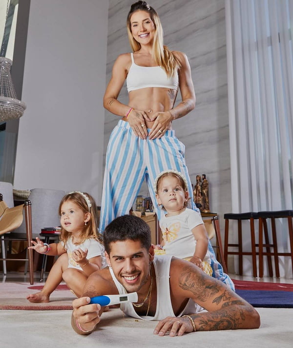foto colorida de virginia fonseca com mão na barriga em pé, ze felipe deitado com teste de gravidez e as duas filhas do casal sentadas perto - metrópoles
