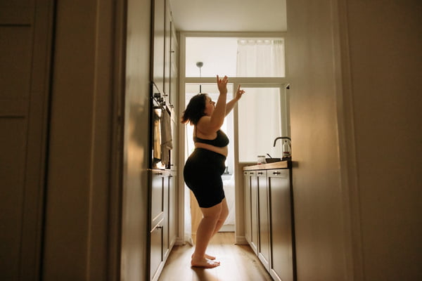 Foto mostra mulher gorda com roupa de ginástica dançando na cozinha de casa