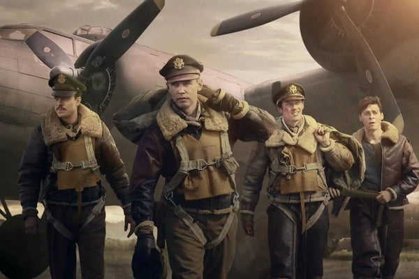 Foto colorida de quatro homens brancos desembarcando para a guerra com uniforme militar verde e um avião ao fundo - Metrópoles