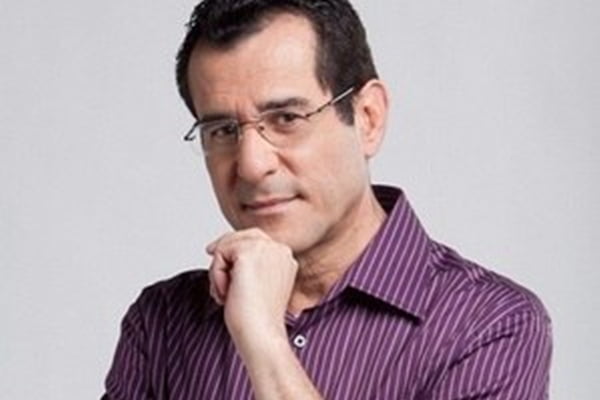 Arnaldo Duran posa, sério, de blusa listrada, óculos e mão no queixo - Metrópoles