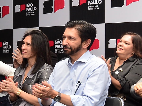 Imagem colorida mostra Ricardo Nunes, de camisa branca, batendo palma sentado e sorrindo - Metrópoles
