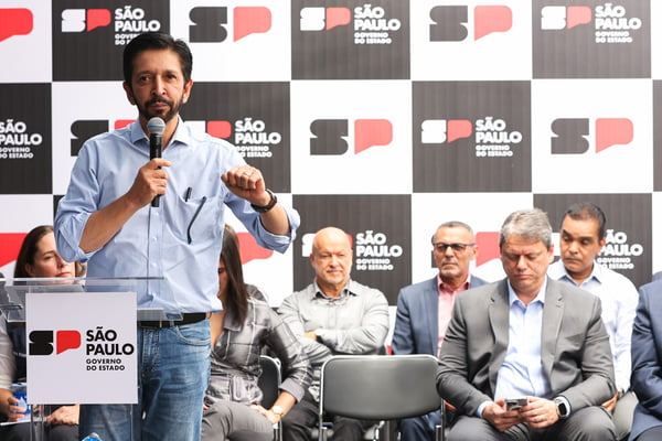 Imagem colorida mostra Ricardo Nunes falando em um palco, na frente de apoiadores