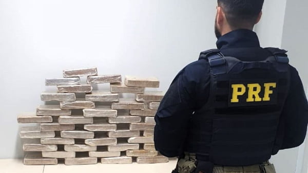 Na imagem, agente da PRF posa ao lado de tabletes de cocaína apreendidos