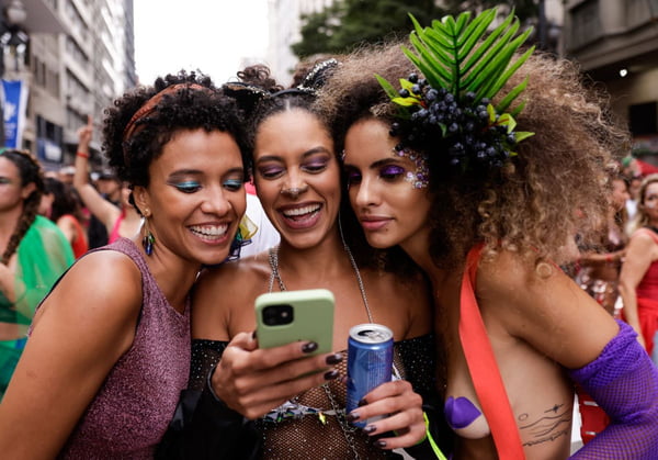 Imagem colorida de mulheres segurando uma latinha e um celular em um bloco de Carnaval, em São Paulo - Metrópoles