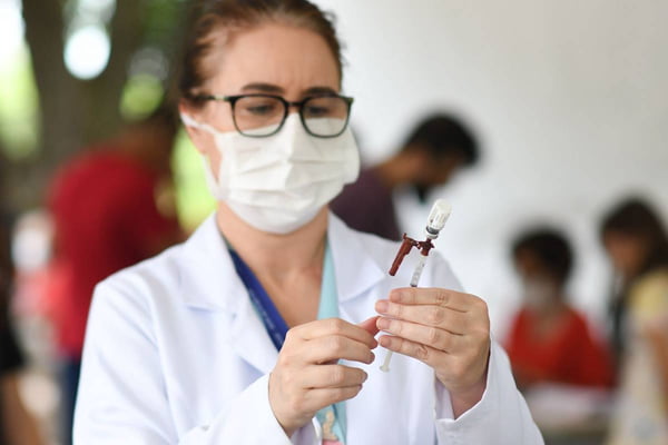 Imagem colorida de mulher preparando vacina. Metrópoles
