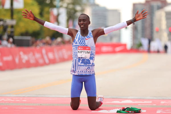 Imagem colorida de maratonosta queniano de joelhos após cruzar a linha de chegada de prova