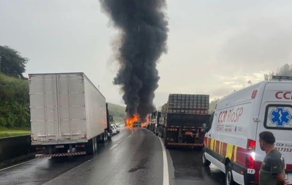 Imagem colorida de carreta que pegando fogo com bastante fumaça e outros caminhões na rodovia Presidente Dutra na região de Queluz em São Paulo - Metrópoles