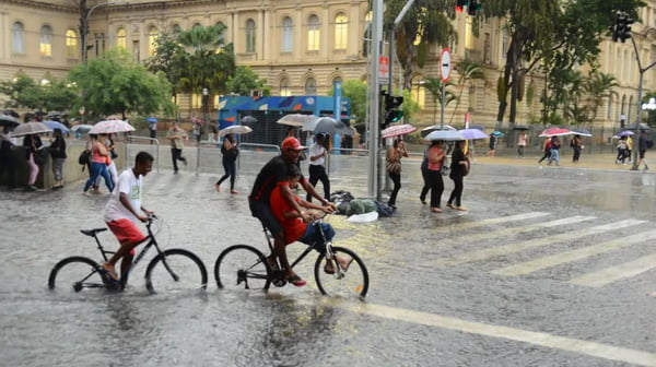 foto colorida de pedestres e ciclistas enfrentando pontos de alagamento no centro de SP durante chuva - Metrópoles