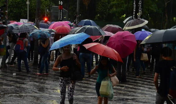 foto colorida de pedestres caminhando com guarda-chuvas em meio à chuva no centro de SP durante chuva - Metrópoles