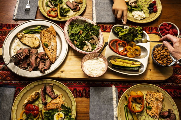 Uma refeição cetogênica disposto sobre uma mesa de jantar com as mãos das pessoas, servindo-se - Metrópoles