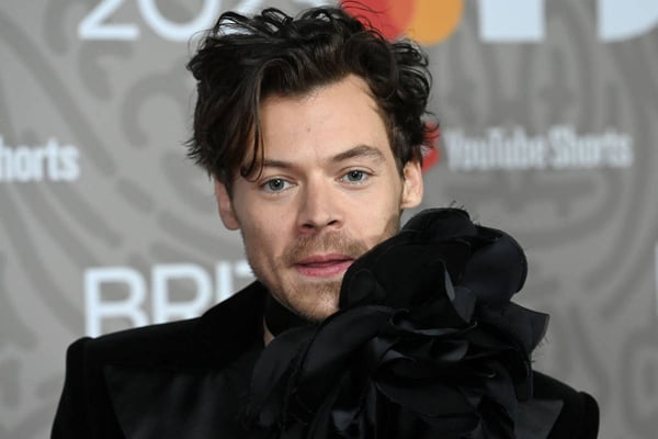 foto colorida do rosto de Harry Styles com blusa preta com flor enorme - metrópoles
