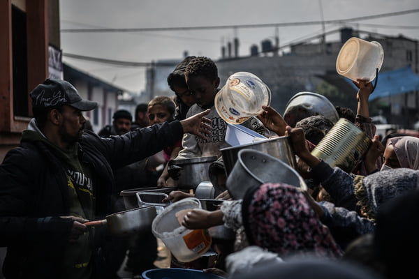 Os palestinos estendem seus recipientes vazios para serem enchidos com alimentos, distribuídos por organizações de caridade em Rafah