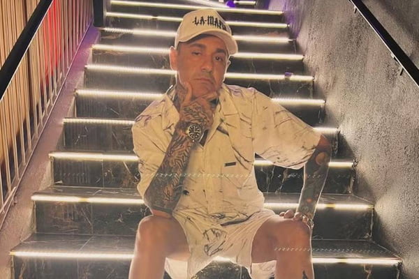 foto colorida de homem de roupa branca e bone sentado em escada - metrópoles