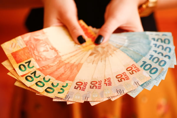 foto colorida de uma mão feminina segurando várias cédulas de dinheiro em real megafeirão - Metrópoles