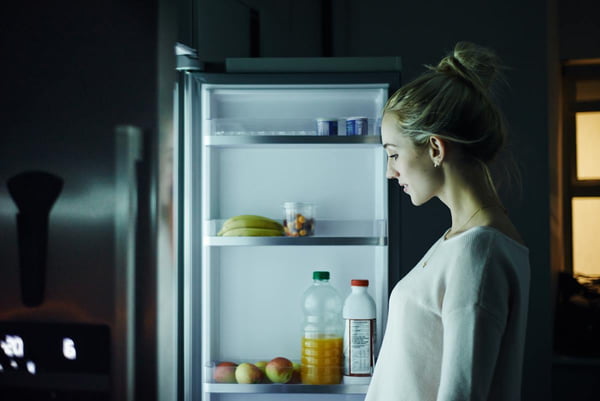 Foto colorida de uma mulher olhando a geladeira - Metrópoles