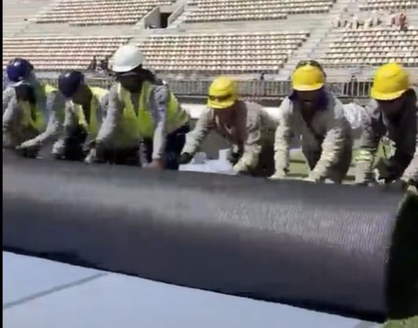 Imagem mostra operários empurrando tapete durante obra no Pacaembu - Metrópoles