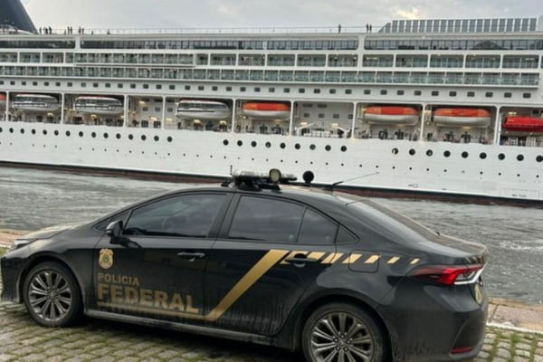Carro preto caracterizado como viatura da Polícia Federal (PF) no primeiro plano. Ao fundo, um navio de cruzeiro.