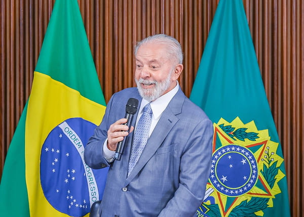 Imagem colorida do presidente Lula, em frente à bandeira do Brasil e segurando microfone - Metrópoles
