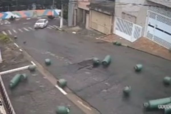 Imagem colorida de botijões de gás rolando por uma rua e um carro branco escapando. Metrópoles