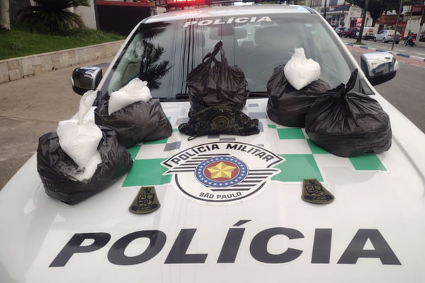 Imagem colorida de sacos plásticos pretos colocados em cima de carro de polícia. Metrópoles