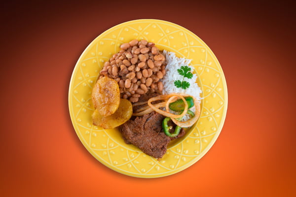 Foto mostra prato amarelo com arroz, feijão, bife, cebola e batatas - Metrópoles