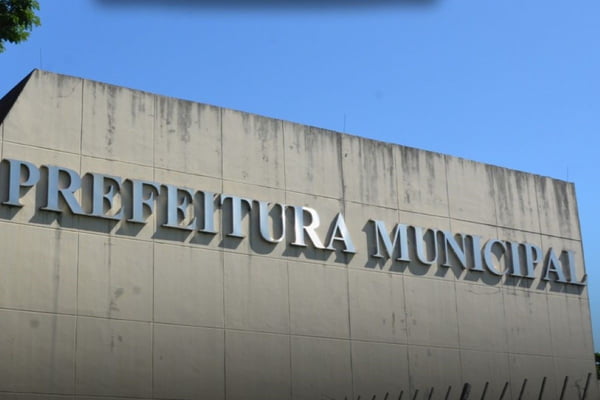 Letreiro escrito "Prefeitura Municipal" em fachada de prédio de concreto, céu azul ao fundo