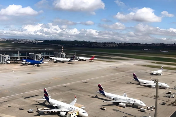 Pista de aeroporto com aeronaves estacionadas, o céu está azul com nuvens