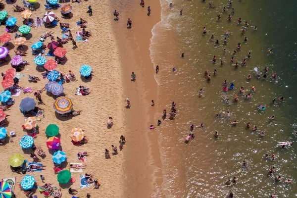 Imagem colorida de praia cheia de banhistas - Metrópoles