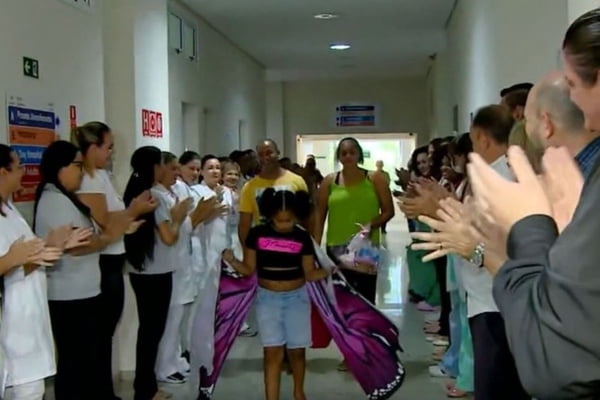 Imagem colorida mostra menina andando em meio a funcionários de hospital - Metrópoles