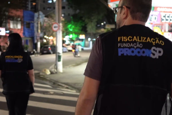 Foto colorida de agentes de fiscalização do Procon com coletes atravessando a rua em São Paulo - Metrópoles