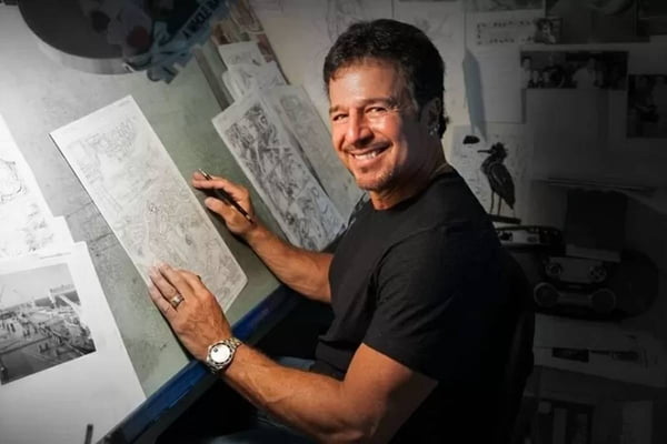Na imagem colorida, homem usa blusa preta, segura lápis e desenha em papéis - Metrópoles