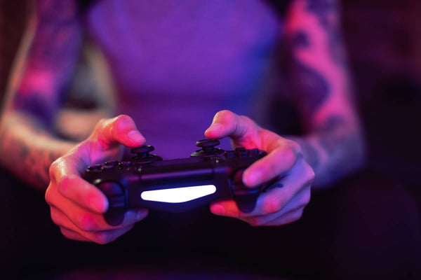 Foto colorida de pessoa branca com braços tatuados jogando jogo eletrônico - Metrópoles