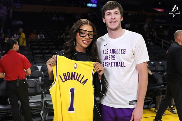 Ludmila segura uma camisa com seu nome e o número um ao lado de jogador dos Lakers