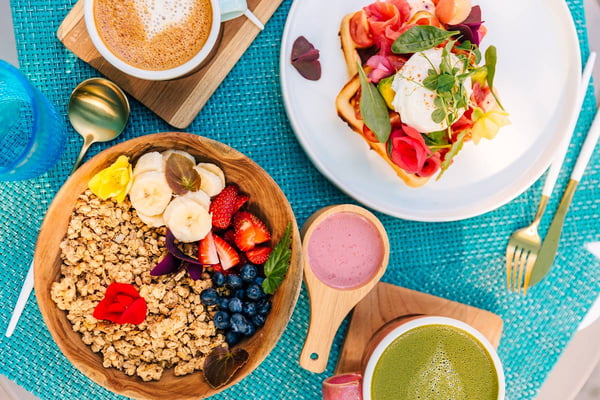 Foto de superfície azul com bowls, xícaras e pratos que trazem comidas dentro, como bruschetta, café , iogurte e frutas - Metrópoles
