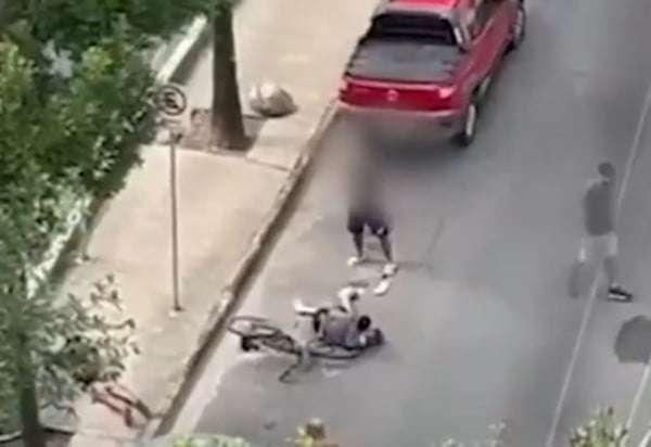 Imagem de homem deitado sobre uma bicicleta na rua enquanto outro, em pé, aponta arma para ele - Metrópoles