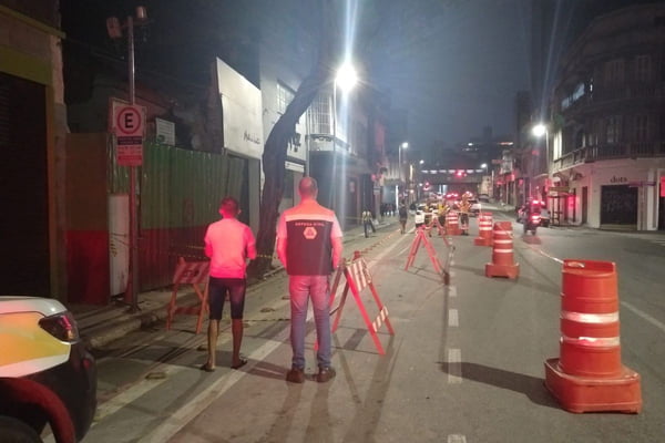 Funcionários da Defesa Civil de colete fazem interdição de rua com cones e cavaletes