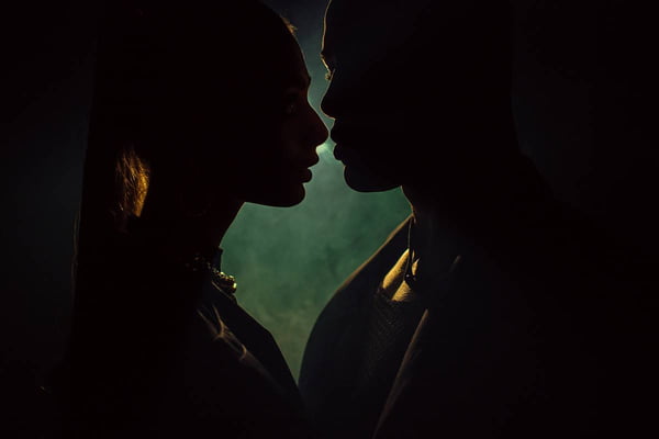 Foto colorida de um casal com os rostos encostadis contra a luz no escuro - Metrópoles